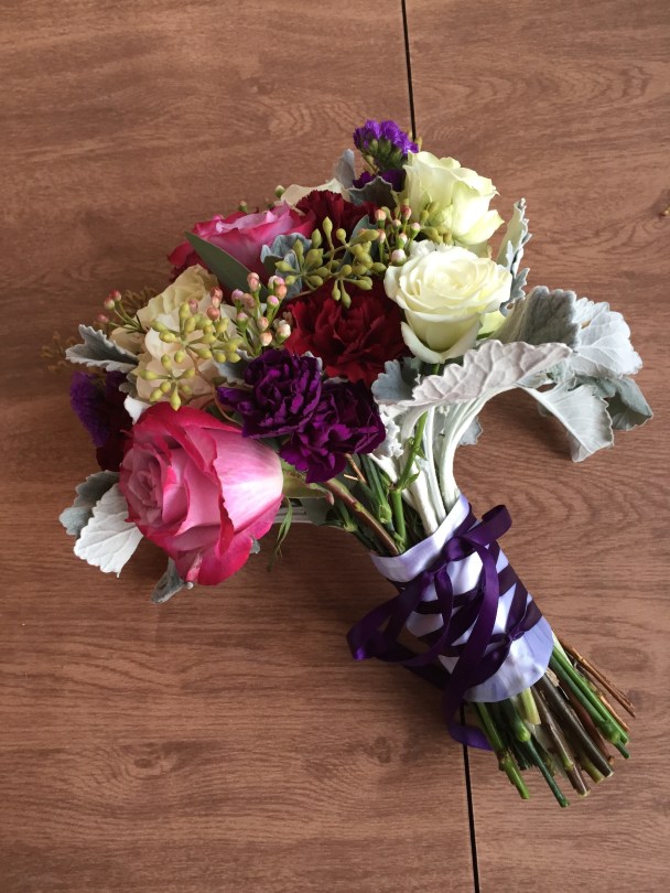 Alaska Winter Wedding | purple roses, plum mini carnations, burgundy carnations, white roses, dusty miller, eucalyptus and wax flower. Bound with white ribbon and a purple corset. Designed by Natasha Price of Alaskaknitnat.com
