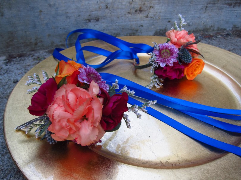 Wrist corsages made with peach mini carnations, orange spray roses, purple button mums and limonium | designed by Natasha Price of Alaskaknitnat.com
